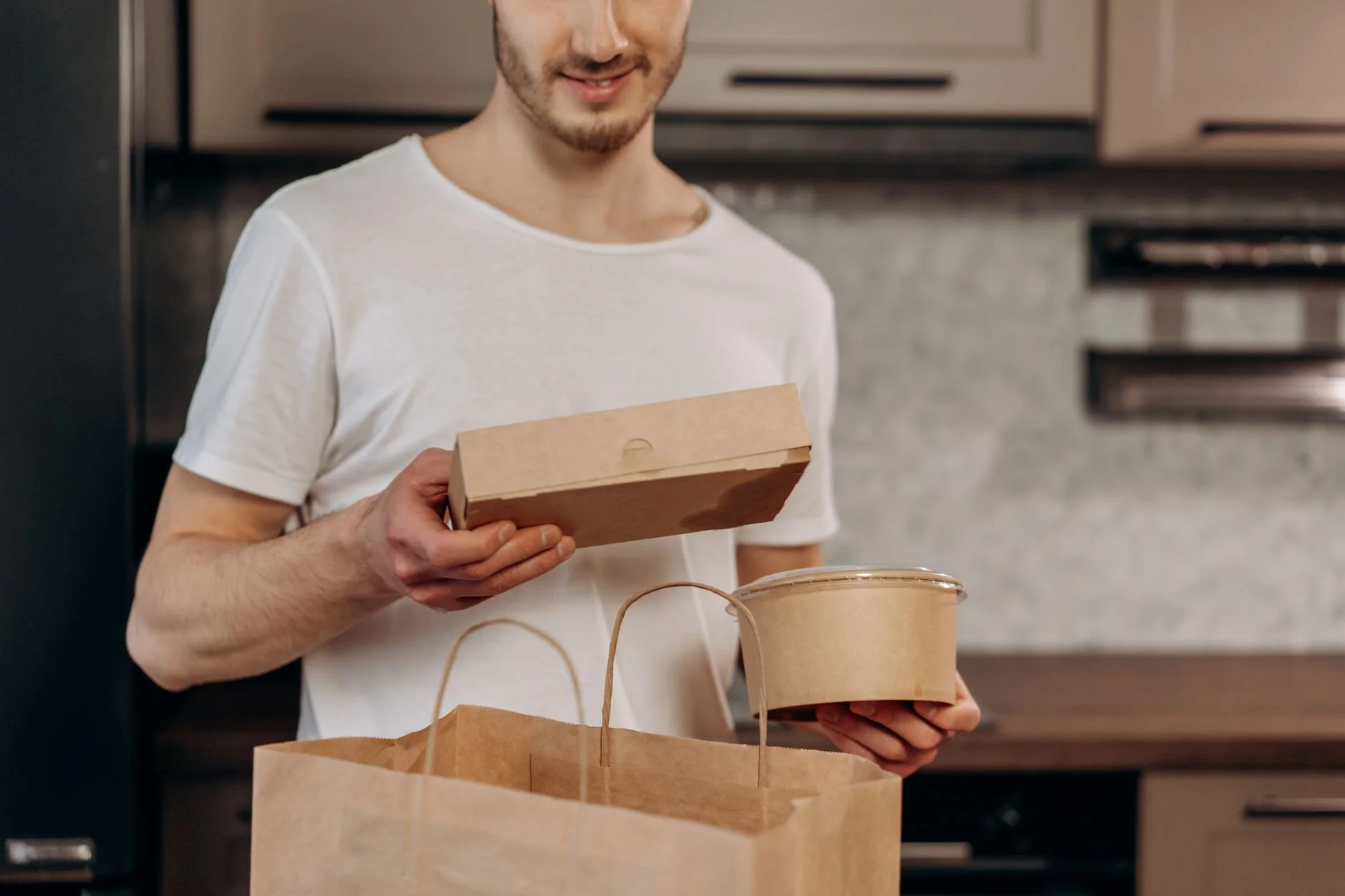 A man in a white shirt manages takeaway food in a kitchen, emphasizing convenience and modern lifestyle.