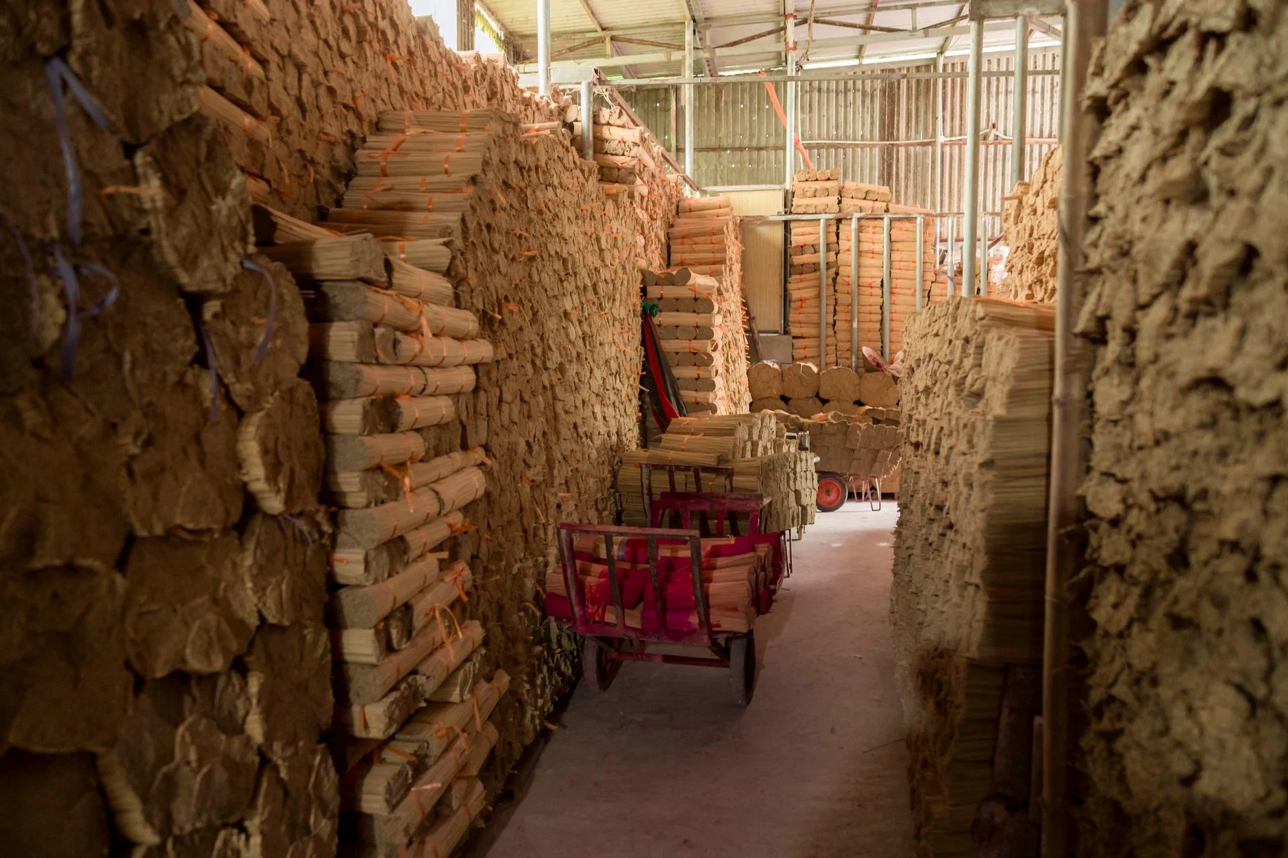 Interior view of a warehouse filled with neatly stacked cardboard bundles and small carts.